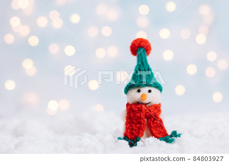 Christmas background with a snowman in a green hat and a red scarf. Greeting card with a happy toy snowman. Happy New Year. Space for text. 84803927