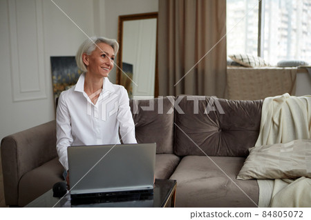 Adult cheerful woman working on laptop at home 84805072