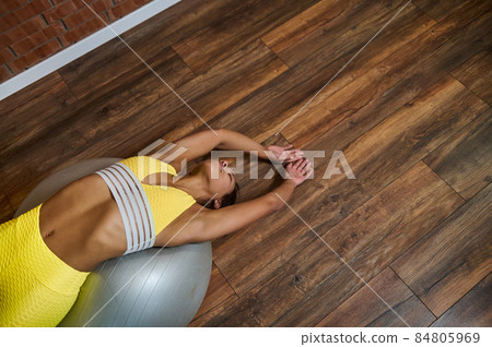 Pilates, fitness, stretching and active lifestyle concept. High angle view of a young woman stretching her body lying on a fitness ball during cross workout 84805969