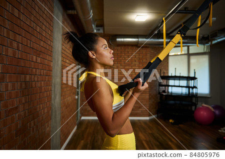 Beautiful African woman doing arm exercises with suspension straps at gym. Sport, resistance, endurance, strength, fitness, active and healthy lifestyle concept 84805976