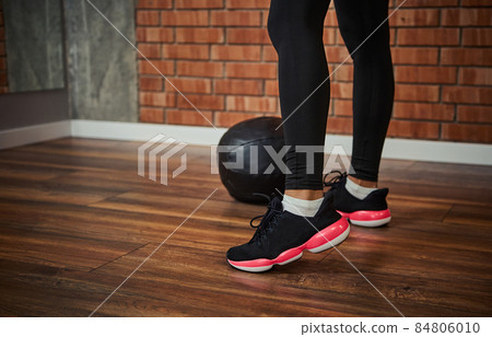 Close-up of female legs in sport shoes next to a medicine ball on the floor against a red bricks wall background with copy space 84806010