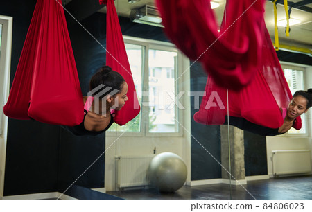 Young African woman doing fly yoga stretching exercises in fitness training at gym hall . Sport and healthy lifestyle concept. Aerial flying yoga class with anti-gravity Young African woman doing fly yoga stretching exercises in fitness training at gym hall . Sport and healthy lifestyle concept. Aerial flying yoga class with anti-gravity 84806023