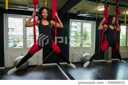 Fit pretty young African womanpracticising aerial fly yoga stretching exercises in a studio. Sport and healthy lifestyle concept Fit pretty young African womanpracticising aerial fly yoga stretching exercises in a studio. Sport and healthy lifestyle concept 84806032