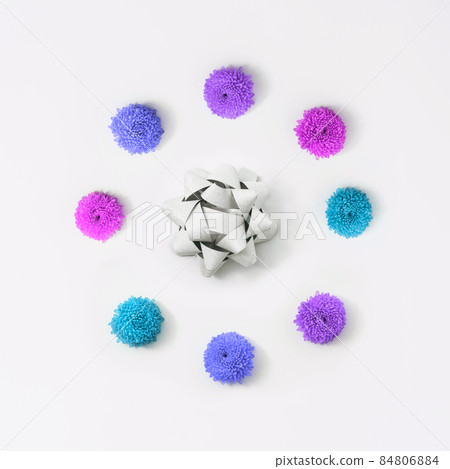A background of chrysanthemums arranged around a silver bow. Postcard with flowers in different neon colors. A background of chrysanthemums arranged around a silver bow. Postcard with flowers in different neon colors. 84806884