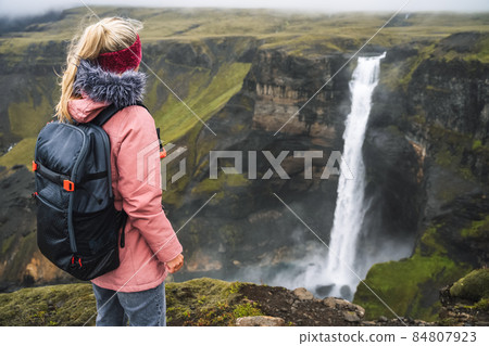 Woman with backpack and lilac jacket enjoying Haifoss waterfall of Iceland Highlands in Thjorsardalur Valley Woman with backpack and lilac jacket enjoying Haifoss waterfall of Iceland Highlands in Thjorsardalur Valley 84807923