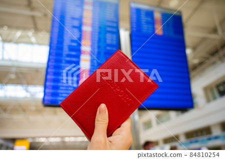 Woman holding a passport against the background of an airport information board. Woman holding a passport against the background of an airport information board. 84810254