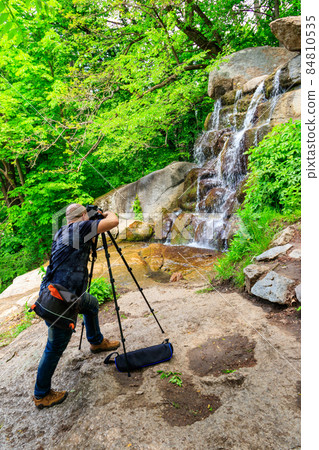 Travel photographer man with professional camera on tripod taking photos of waterfall 84810535