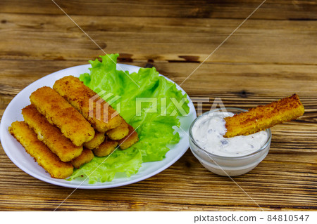Fried fish fingers on a plate with lettuce and tartar sauce on wooden table 84810547