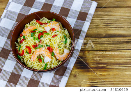 Bowl of instant Chinese noodles with shrimps, green onion and red hot chilli peppers on wooden table. Top view 84810629