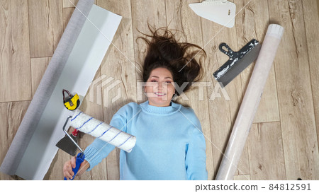Woman lies holding roller among materials scattered on floor Woman lies holding roller among materials scattered on floor 84812591