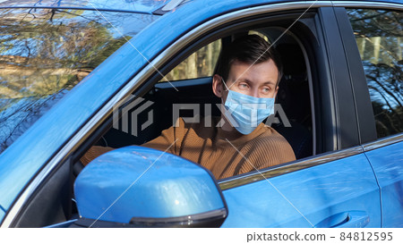 Man with dark hair in medical mask sits in car on roadside near forest 84812595