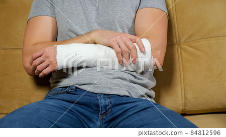 Man touches injured arm in gypsum band and sighs tiredly 84812596