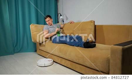 Robot vacuum cleaner delivers alcohol to man sitting on sofa Robot vacuum cleaner delivers alcohol to man sitting on sofa 84812727