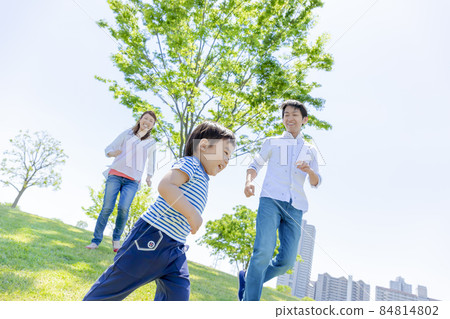 Three-person family playing in a fresh green park 84814802