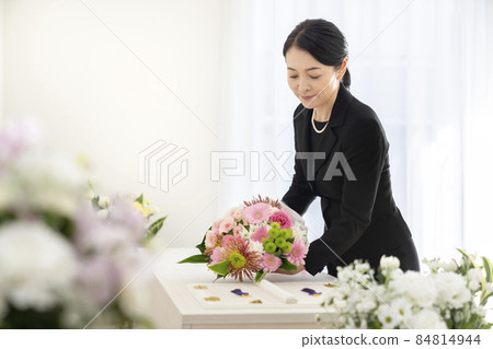 Middle-aged woman offering a bouquet to the casket 84814944