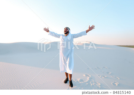 Happy Muslim man looks through banknotes and beside himself with joy, standing in center of sandy desert on warm, hot day. Happy Muslim man looks through banknotes and beside himself with joy, standing in center of sandy desert on warm, hot day. 84815140