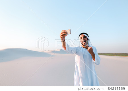 Portrait of Arabian sheikh man with gadget that communicates in skype against blue sky on summer day. 84815169