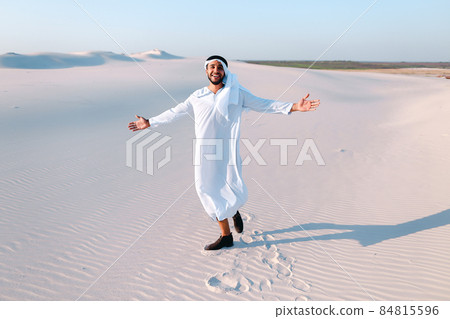Happy Arab man walks in middle of white desert and enjoys life on hot summer day. 84815596