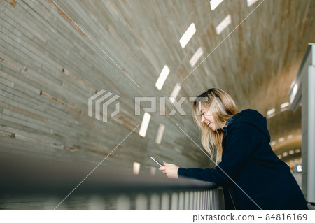 Blonde girl standing with modern smartphone in monophonic illumi 84816169