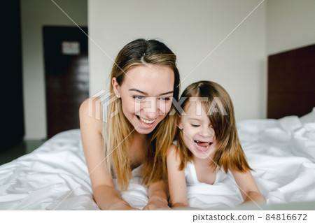 Young woman lying in bed with little daughter in morning. 84816672