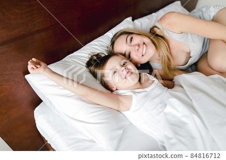 Happy mother lying in bed with little jocund daughter. Happy mother lying in bed with little jocund daughter. 84816712