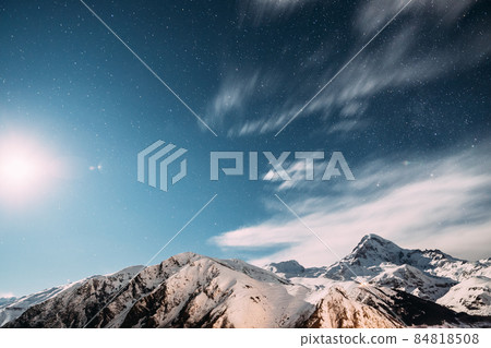 Stepantsminda, Georgia. Moonrise In Winter Night Starry Sky With Glowing Stars Over Peak Of Mount Kazbek Covered With Snow. Beautiful Night Georgian Winter Landscape 84818508