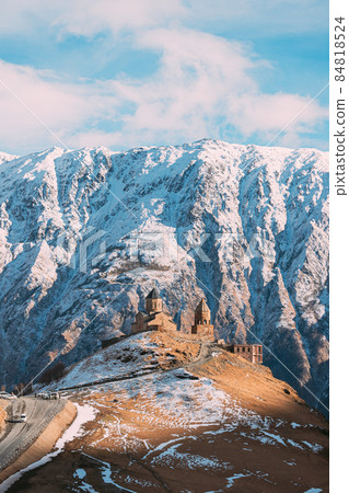 Stepantsminda, Georgia. Famous Gergeti Trinity Tsminda Sameba Church In Early Winter Landscape. Beautiful Georgian Mountains Landscape Stepantsminda, Georgia. Famous Gergeti Trinity Tsminda Sameba Church In Early Winter Landscape. Beautiful Georgian Mountains Landscape 84818524