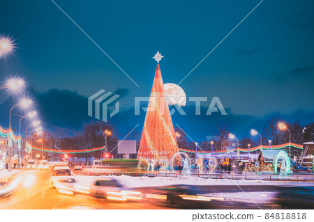 Gomel, Belarus. Main Christmas Tree And Festive Illumination On Lenin Square In Gomel. New Year In Belarus. Altered Night Sky With Moon Gomel, Belarus. Main Christmas Tree And Festive Illumination On Lenin Square In Gomel. New Year In Belarus. Altered Night Sky With Moon 84818818