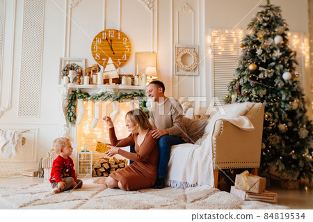 mom and dad give box with a gift to little son in room decorated for new year mom and dad give box with a gift to little son in room decorated for new year 84819534