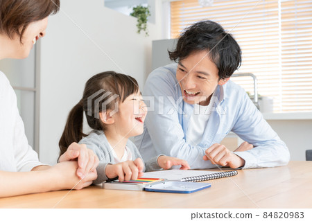 Elementary school girl and dad with missing upper front teeth laughing while drawing in the living room 84820983