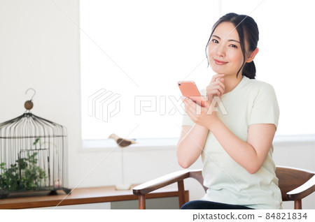 一個女人坐在椅子上操作智能手機 一個女人坐在椅子上操作智能手機 84821834