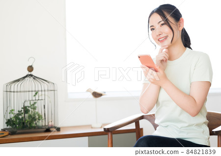 一個女人坐在椅子上操作智能手機 一個女人坐在椅子上操作智能手機 84821839