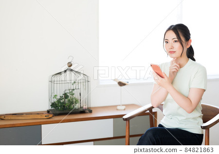 一個女人坐在椅子上操作智能手機 一個女人坐在椅子上操作智能手機 84821863