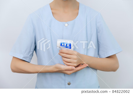 Temperature measurement gun in doctor hands. Close-up shot of doctor wearing protective surgical mask ready to use infrared isometric thermometer gun to check body temperature for virus symptoms. Temperature measurement gun in doctor hands. Close-up shot of doctor wearing protective surgical mask ready to use infrared isometric thermometer gun to check body temperature for virus symptoms. 84822002