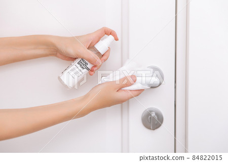 Cleaning white door handles with an antiseptic wet wipe and sanitizer spray. Disinfection in hospital and public spaces against corona virus. Woman hand using towel for cleaning home room door link. Cleaning white door handles with an antiseptic wet wipe and sanitizer spray. Disinfection in hospital and public spaces against corona virus. Woman hand using towel for cleaning home room door link. 84822015