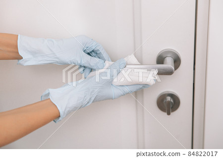 Cleaning black door handles with an antiseptic wet wipe in blue gloves. Sanitize surfaces prevention in hospital and public spaces against corona virus. Woman hand using towel for cleaning. Cleaning black door handles with an antiseptic wet wipe in blue gloves. Sanitize surfaces prevention in hospital and public spaces against corona virus. Woman hand using towel for cleaning. 84822017