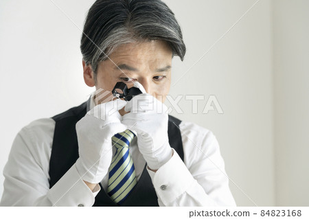 Image of a middle-aged male jewel appraiser looking at a ring with a loupe 84823168