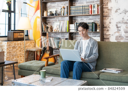 A young man working on a computer with his laptop on his lap in the living room 84824509