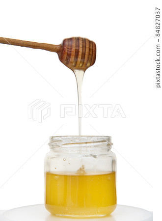 Dripping honey from honey dipper into jar of organic healthy sweet natural honey, isolated over white background with copy space 84827037