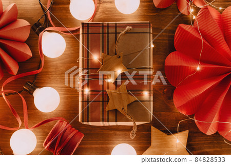 Gift wrapped with kraft paper and Christmas lights on wooden table, sustainable decorations, 84828533