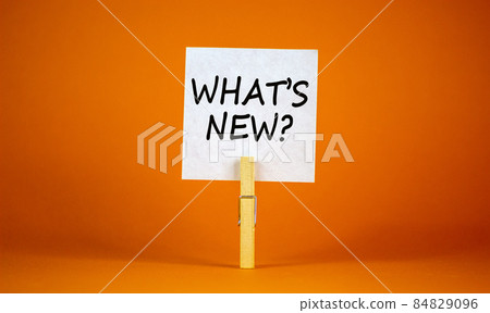 What is new symbol. White sheet of paper on wooden clothespin. Words 'what is new'. Beautiful orange background. Business and what is new concept, copy space. 84829096