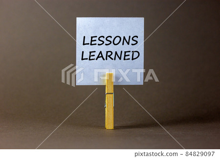White paper with text 'lessons learned', clip on wood clothespin. Beautiful grey background. Business concept. Copy space. 84829097