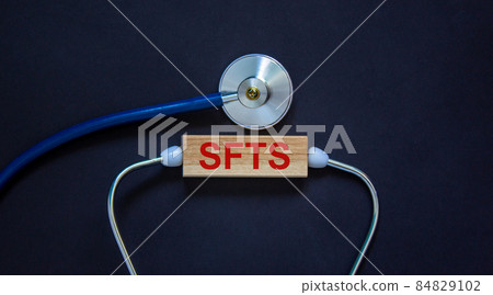COVID-19 Pandemic Coronavirus and medical concept. Wooden block with the inscription 'SFTS' and stethoscope. Beautiful black background. 84829102