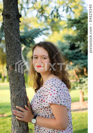 Young brunette girl in dress is posing on tree background in the summer in park 84829340