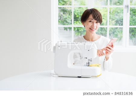 A woman who operates a sewing machine while looking at a smartphone A woman who operates a sewing machine while looking at a smartphone 84831636