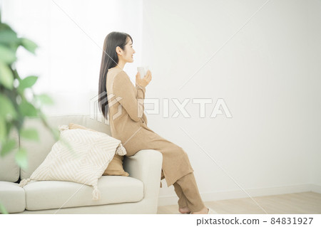 A woman sitting on the sofa while drinking coffee (drink) 84831927