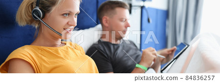 Woman in headphones lying in bed and working at laptop next to man with tablet Woman in headphones lying in bed and working at laptop next to man with tablet 84836257