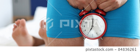 Man holding alarm clock near genitals against background of lying female legs closeup Man holding alarm clock near genitals against background of lying female legs closeup 84836261