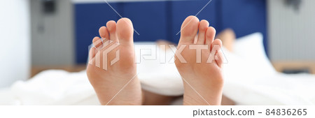 Female feet lying on white bed under covers closeup Female feet lying on white bed under covers closeup 84836265