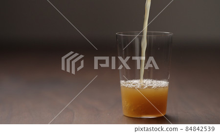 pour orange detox drink into tumbler glass on wood table 84842539